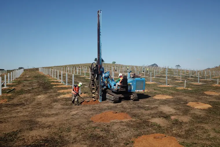 Cravação de estacas em usina fotovoltaica, com equipe uniformizada e estacas já cravadas ao fundo
